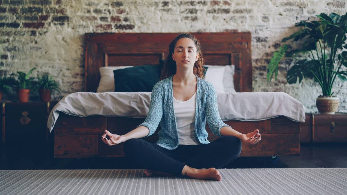 Woman practicing mental stress reduction techniques by sitting calmly in a park with eyes closed, hands resting on knees